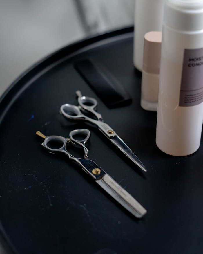 Set of professional haircut tools and moisturizing shampoo bottle on a black tray, ready for salon use.