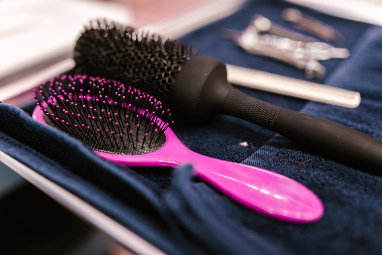 Close-up of pink and black hairbrushes on a towel in a salon setting.